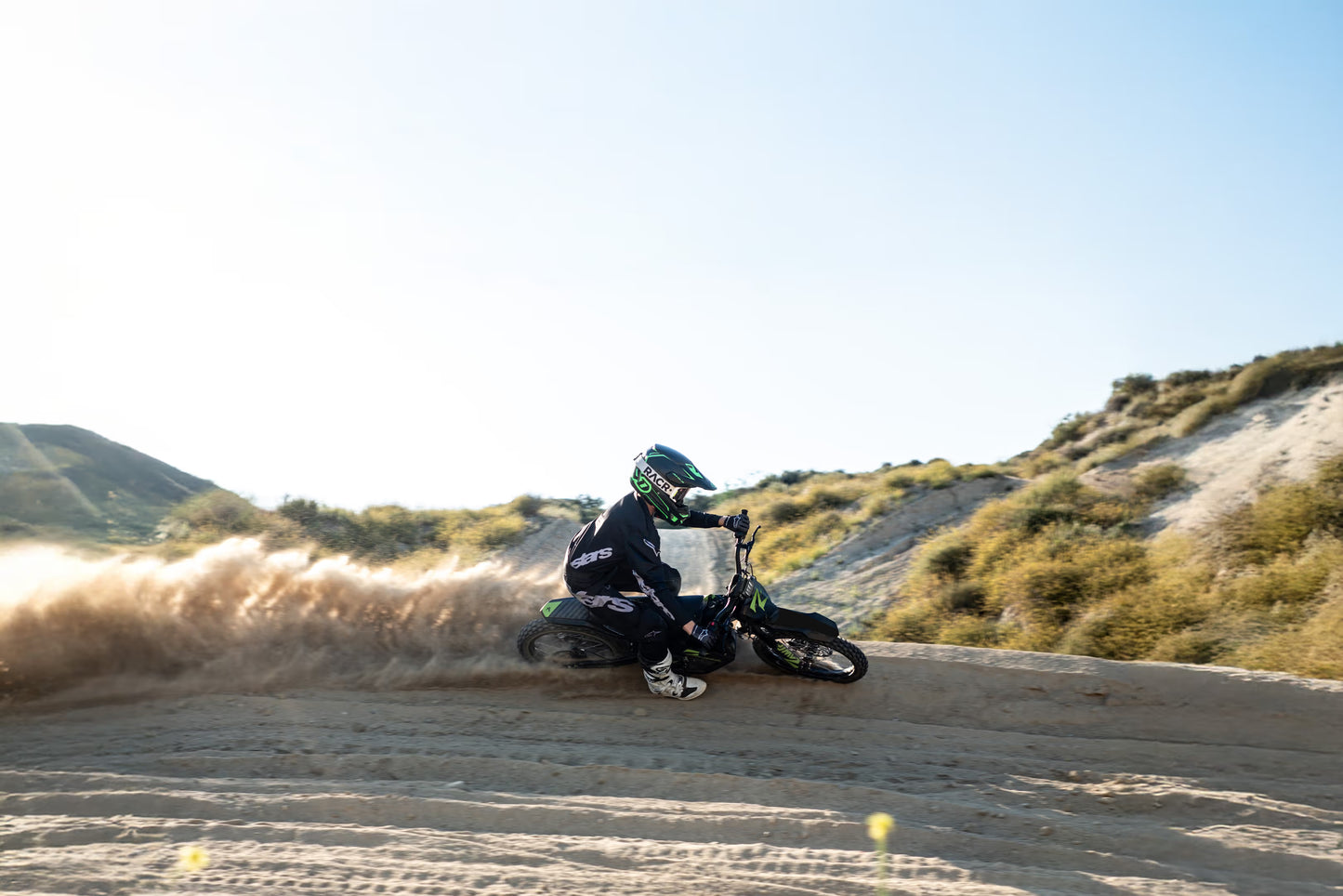 Person riding a dirt bike on a sandy track with a clear sky