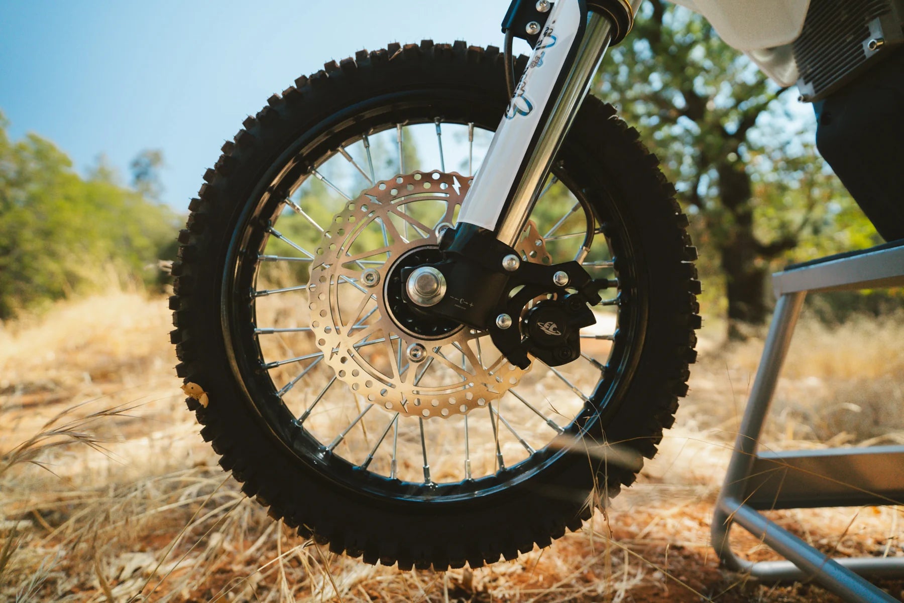 Close-up of a motorcycle wheel in an outdoor setting with trees and grass.